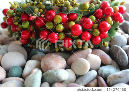 Ornamental Garland With Plastic Berries And Fabric Leaves Lying On Colored Sea Stones Ornamental Garland With Plastic Berries And Fabric Leaves Lying On Colored Sea Stones 134270468