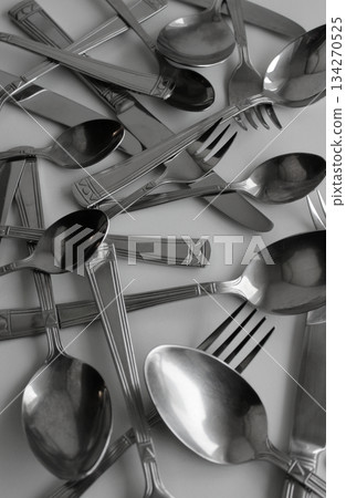 Used stainless steel forks, spoons and knives scattered on white surface vertical stock photo 134270525