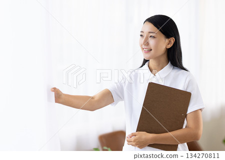 A woman in a white coat smiling and opening the curtains A woman in a white coat smiling and opening the curtains 134270811