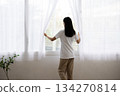 Back view of a woman in a white coat opening the curtain 134270814