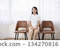 A woman in a white coat sitting in a chair by the window and smiling 134270816