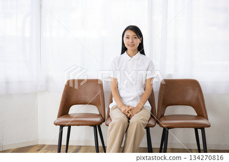 一位身穿白大褂的女士坐在窗邊的椅子上，面帶微笑。 134270816