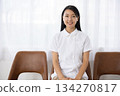A woman in a white coat sitting in a chair by the window and smiling 134270817