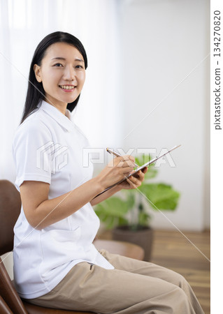 一位身穿白大褂的女士面帶微笑地做著筆記。 134270820