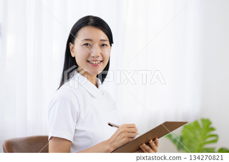 一位身穿白大褂的女士面帶微笑地做著筆記。 134270821