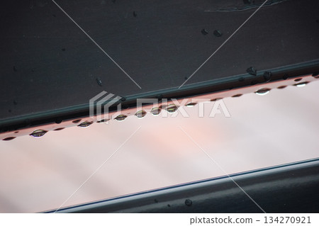 Macro image of water droplets hanging from a dark surface with a subtle pink reflection below 134270921