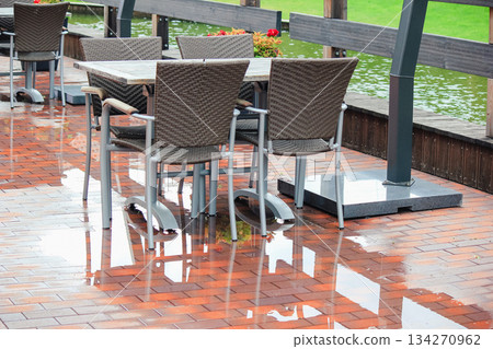 Empty wicker chairs and tables on a wet cafe patio reflecting in the brick pavement after rain Empty wicker chairs and tables on a wet cafe patio reflecting in the brick pavement after rain 134270962