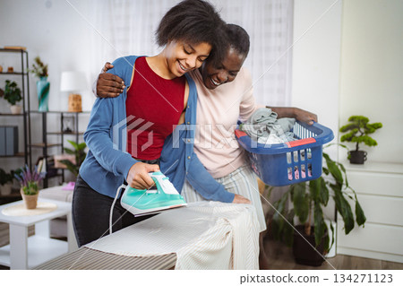 Two cheerful black girls ironing clothes and having fun at home Two cheerful black girls ironing clothes and having fun at home 134271123