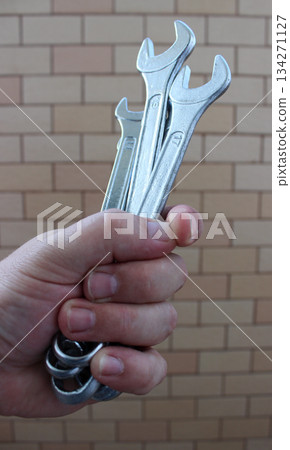 Clenched Human Fist With Different Open End Wrenches Over Brick Wall 134271127