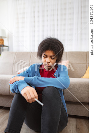 Sad teenage girl sitting on the floor at home holding a pregnancy test 134271142