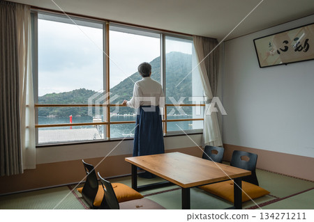 Japanese-style room with an elderly woman looking out the window at the sea Japanese-style room with an elderly woman looking out the window at the sea 134271211