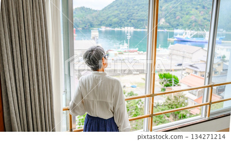 一位老婦人背對著鏡頭,望著窗外的大海。 一位老婦人背對著鏡頭,望著窗外的大海。 134271214