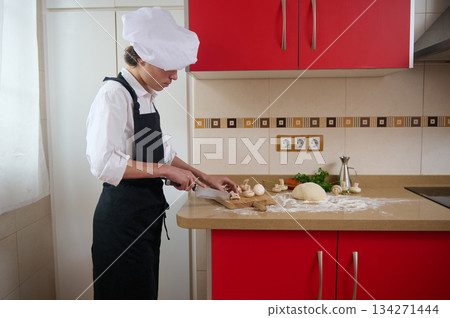 Chef In White Shirt And Black Apron Chopping Mushrooms In Red Kitchen 134271444