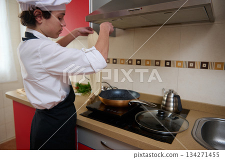 Young Chef Tossing Pizza Dough in Modern Kitchen While Cooking on Stovetop 134271455