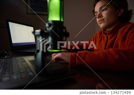 Young Boy Recording Podcast At Home With Laptop And Green Microphone Studio Setup Night Lights Young Boy Recording Podcast At Home With Laptop And Green Microphone Studio Setup Night Lights 134271489