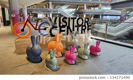 A vibrant visitor centre display with colorful rabbits, a stylized bicycle, and gradient pillars creates a playful, A vibrant visitor centre display with colorful rabbits, a stylized bicycle, and gradient pillars creates a playful, 134271490
