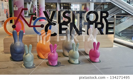 A vibrant visitor centre display with colorful rabbits, a stylized bicycle, and gradient pillars creates a playful, A vibrant visitor centre display with colorful rabbits, a stylized bicycle, and gradient pillars creates a playful, 134271495