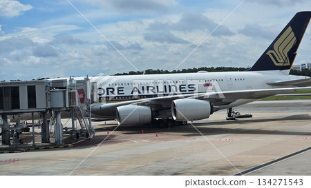 A Singapore Airlines jet stands at the gate with ground vehicles and cargo nearby, showcasing sleek design, global connectivity 134271543
