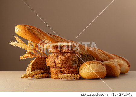Sliced bread, baguette, and French buns with wheat ears on a beige background. 134271743
