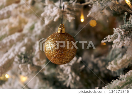 Golden glitter christmas ornament ball hanging on a flocked christmas tree. New Year decoration for holiday season. Golden glitter christmas ornament ball hanging on a flocked christmas tree. New Year decoration for holiday season. 134271846