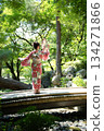 A woman in a yukata holding a folding fan on a bridge in a garden with fresh greenery. Kyoto City, Kyoto Prefecture, Japan 134271866