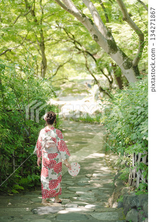 A woman in a red yukata walking along a forest path in summer, holding a fan. Kyoto City, Kyoto Prefecture, Japan 134271867