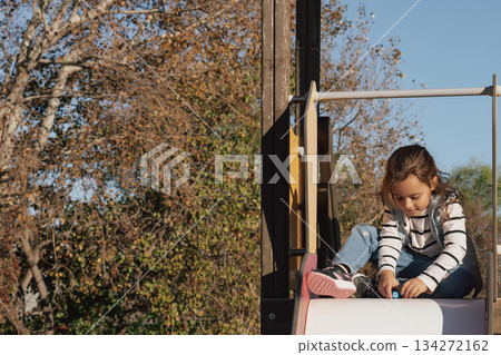 Childhood moments: a contented girl with her toys on a playground slide in the sun 134272162