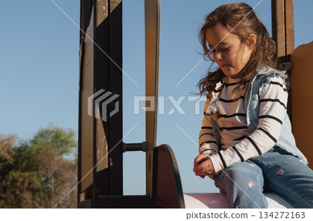Childhood moments: a contented girl with her toys on a playground slide in the sun Childhood moments: a contented girl with her toys on a playground slide in the sun 134272163