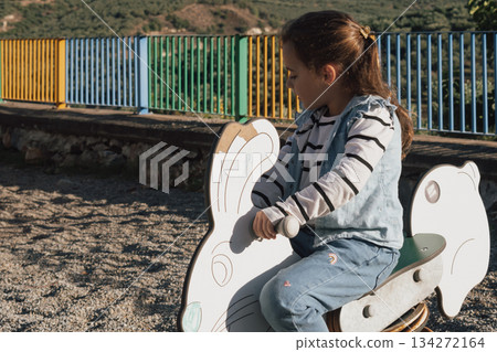Playground fun: a child on a colourful spring toy in the shape of a bunny or rabbit Playground fun: a child on a colourful spring toy in the shape of a bunny or rabbit 134272164