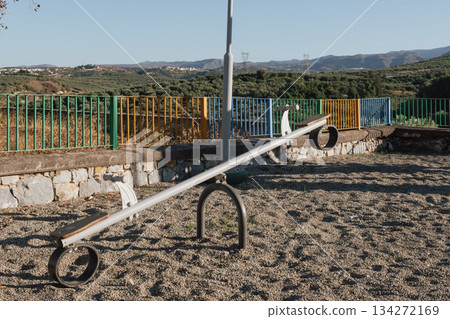 Play equipment: empty face-to-face swing at a sunny park, backed by olive trees 134272169