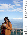 Young woman using smartphone while standing against a scenic Himalayan mountain backdrop 134272577