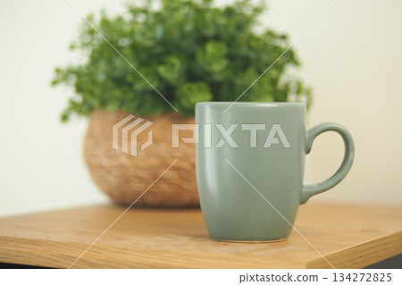 Warm drink sits beside plant on wooden table 134272825
