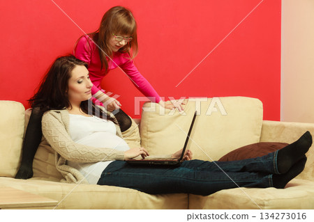 Pregnant woman and daughter sitting with laptop Pregnant woman and daughter sitting with laptop 134273016