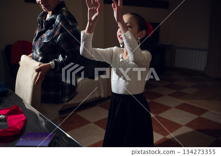 Young Girl Dances With Raised Hands In Home Setting, Guided By Caring Adult During Holiday Prep Young Girl Dances With Raised Hands In Home Setting, Guided By Caring Adult During Holiday Prep 134273355