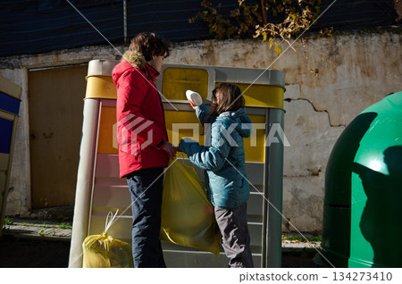 Two People In Winter Jackets Sorting Recyclables At A Colorful Public Recycling Bin Two People In Winter Jackets Sorting Recyclables At A Colorful Public Recycling Bin 134273410