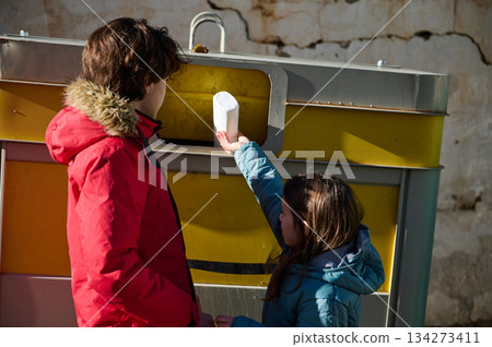 Mother And Daughter Recycling Paper At Large Yellow Recycling Bin In City Street 134273411