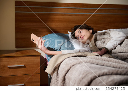 Woman Lying In Bed Taking Selfie With Phone In Cozy Bedroom At Night Woman Lying In Bed Taking Selfie With Phone In Cozy Bedroom At Night 134273425