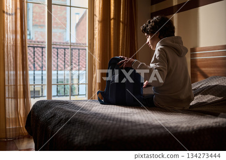 Young Boy Packing Backpack on Bed in Sunny Bedroom With Morning Light Young Boy Packing Backpack on Bed in Sunny Bedroom With Morning Light 134273444
