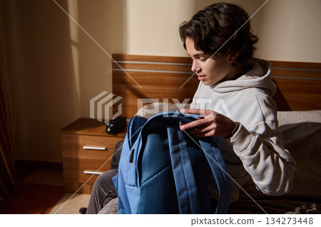 Young Man Packing A Backpack In A Cozy Bedroom Morning Scene, Focused And Calm 134273448