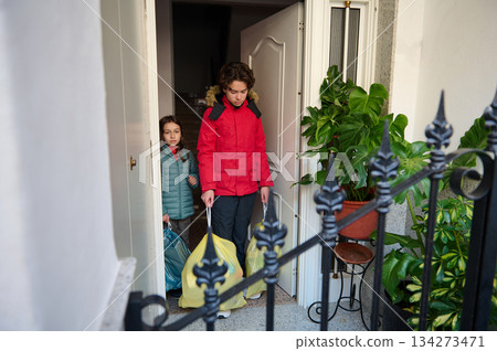 Children Carry Bags at Front Door After Shopping, Red and Teal Jackets, Home Entrance 134273471