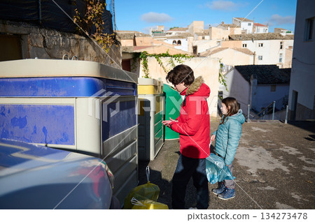 Children In Winter Coats Recycle Near Colorful Bins In Quiet Urban Alley Children In Winter Coats Recycle Near Colorful Bins In Quiet Urban Alley 134273478