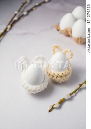 Easter background. willow seals, white egg in a knitted bunny egg holder. Spring time. Minimalistic 134274216
