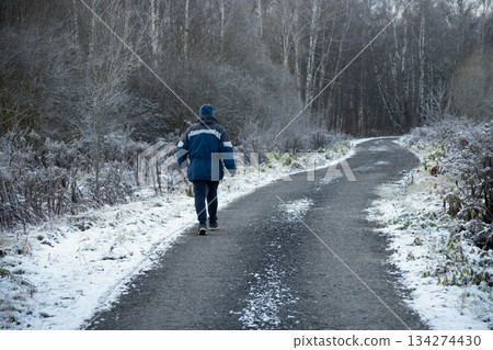 Senior caucasian man walking alone along a snowy rural road in winter forest. Concept of solitude, journey, healthy lifestyle and active aging. Senior caucasian man walking alone along a snowy rural road in winter forest. Concept of solitude, journey, healthy lifestyle and active aging. 134274430