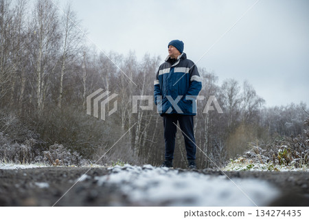 Adult happy man walks in winter park wearing blue sports jacket. Winter walk in frosty forest. Healthy season lifestyle. Outdoors. Adult happy man walks in winter park wearing blue sports jacket. Winter walk in frosty forest. Healthy season lifestyle. Outdoors. 134274435
