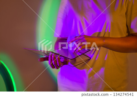 Stunning fusion woman in white shirt with laptop in inspired colorful illuminationt. Slim woman in white shirt with digital tablet under bright saturated neon light. Stunning fusion woman in white shirt with laptop in inspired colorful illuminationt. Slim woman in white shirt with digital tablet under bright saturated neon light. 134274541