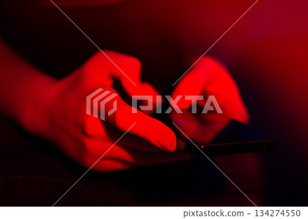 Cropped woman hand using smartphone on a neon glowing background. Happy young girl looking at screen close. 134274550