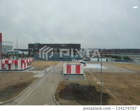 An emergency medical services helicopter is parked on the helipad ready for takeoff against the backdrop of a modern hospital building under a cloudy sky A medical helicopter on the hospital grounds. 134274787