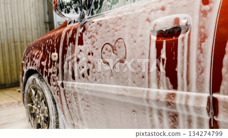 Red car door with soap heart, full side panel coated in thick foam with alloy wheel visible, detailerready lather creating contrast with glossy paint, commercial wash bay vibe, satisfying aftercare 134274799