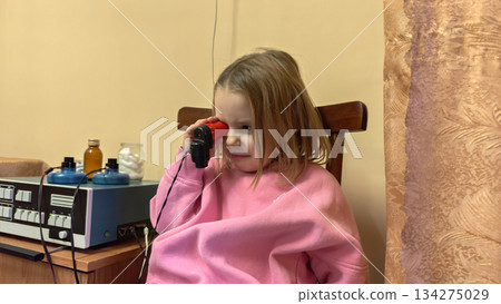 A child undergoes magnetic therapy for eye treatment at a children's clinic The child sits quietly during a physical therapy session holding the device in his hands during ophthalmological treatment. 134275029