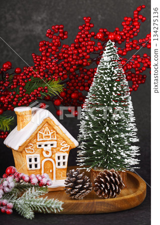 Gingerbread style ceramic Christmas house with ornaments, holly berries and snowy winter tree 134275136